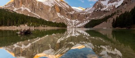 Paisaje montañoso con un lago que refleja las montañas y un pequeño bote en el agua.
