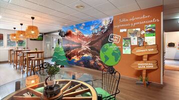 A modern hotel lobby with a large mural, wooden furniture, and a glass table with a wooden wheel centerpiece.