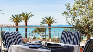 A dining table with a view of the sea, striped chairs, and a palm tree. - Hotel Princess (Bar)
