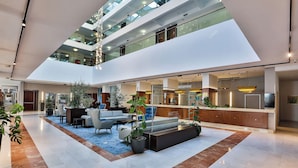 A modern hotel lobby with a reception desk, seating area, and a staircase leading to upper floors. - Hotel Princess (Bar)