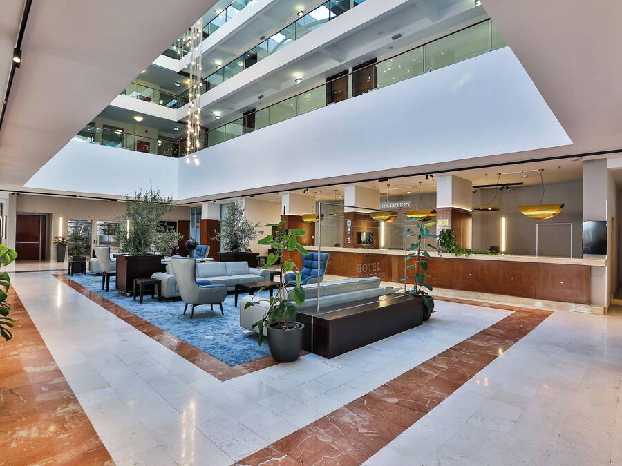 A modern hotel lobby with a reception desk, seating area, and a staircase leading to upper floors.