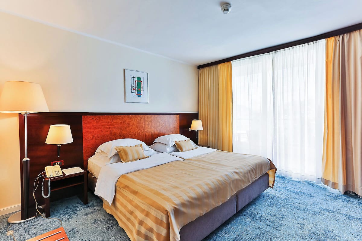 A hotel room with a large bed, two bedside tables, a desk with a telephone, and a window with curtains.
