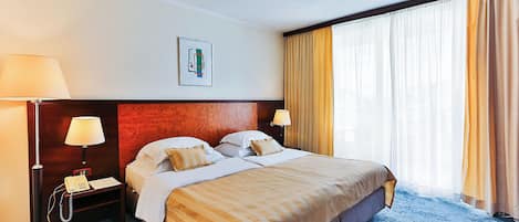 Habitación de hotel con una cama grande, dos mesitas de noche, un escritorio con teléfono y una ventana con cortinas.
