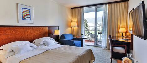 A hotel room with a bed, a desk, a chair, a TV, and a balcony with curtains.