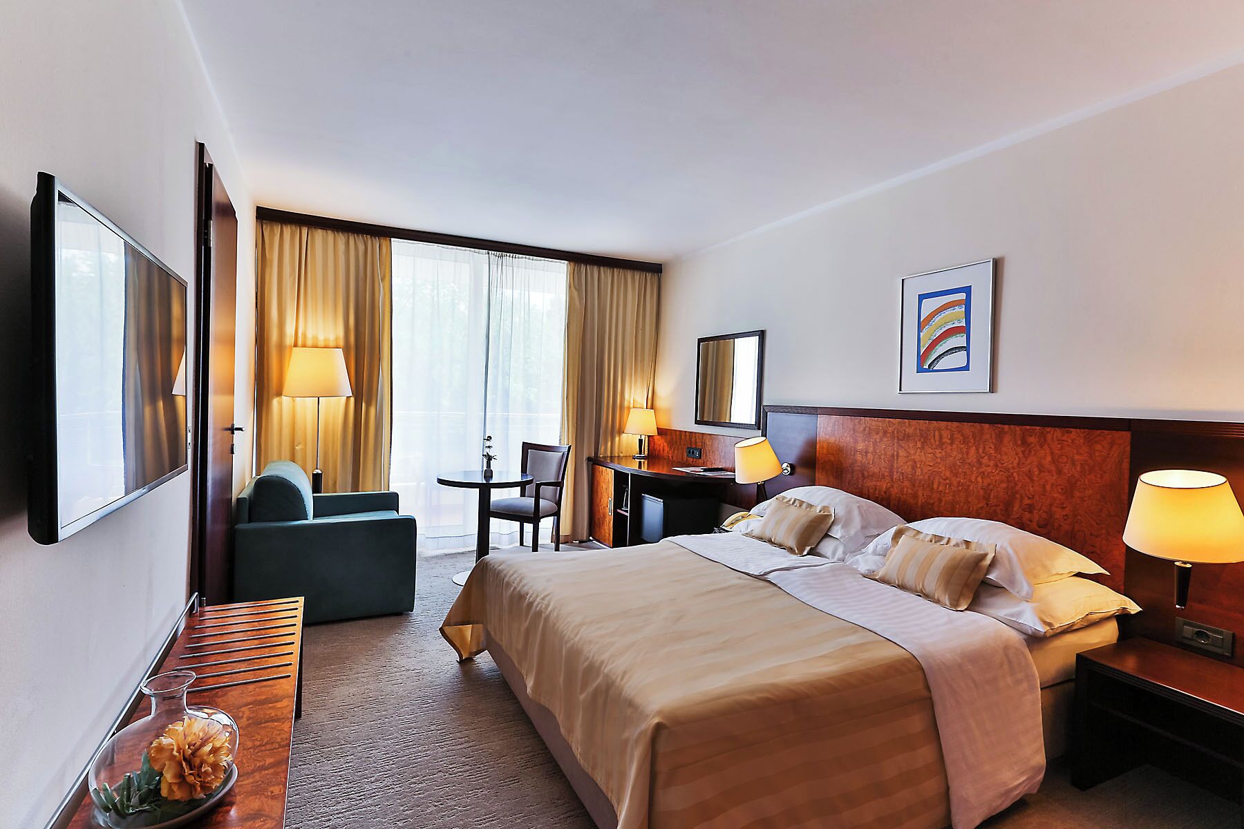 A hotel room with a large bed, a desk, a chair, a TV, and a window with curtains.