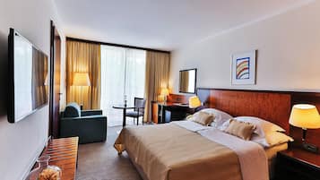 Quarto de hotel com uma cama grande, uma escrivaninha, uma cadeira, uma televisão e uma janela com cortinas.