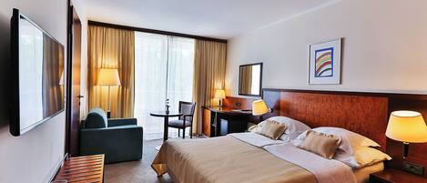 A hotel room with a large bed, a desk, a chair, a TV, and a window with curtains.