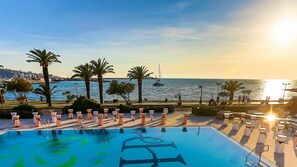A pool with a view of the sea and boats, surrounded by palm trees and outdoor seating. - Hotel Princess (Bar)