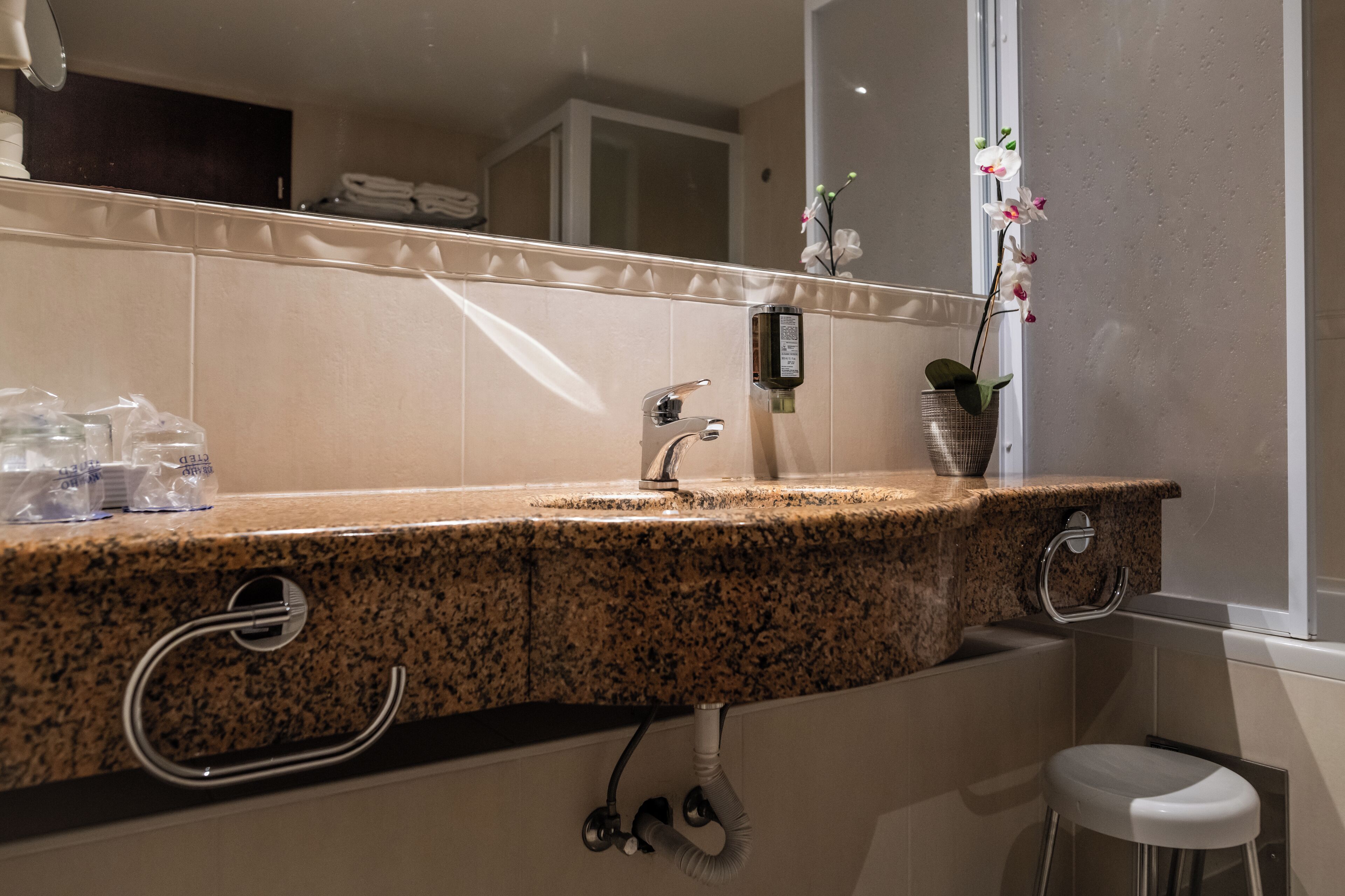 A bathroom with a granite countertop, a mirror, a towel rack, a sink, a toilet, and a small stool.