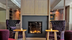 Un rincón acogedor con chimenea, dos mesas de madera y sillones tapizados de color púrpura.