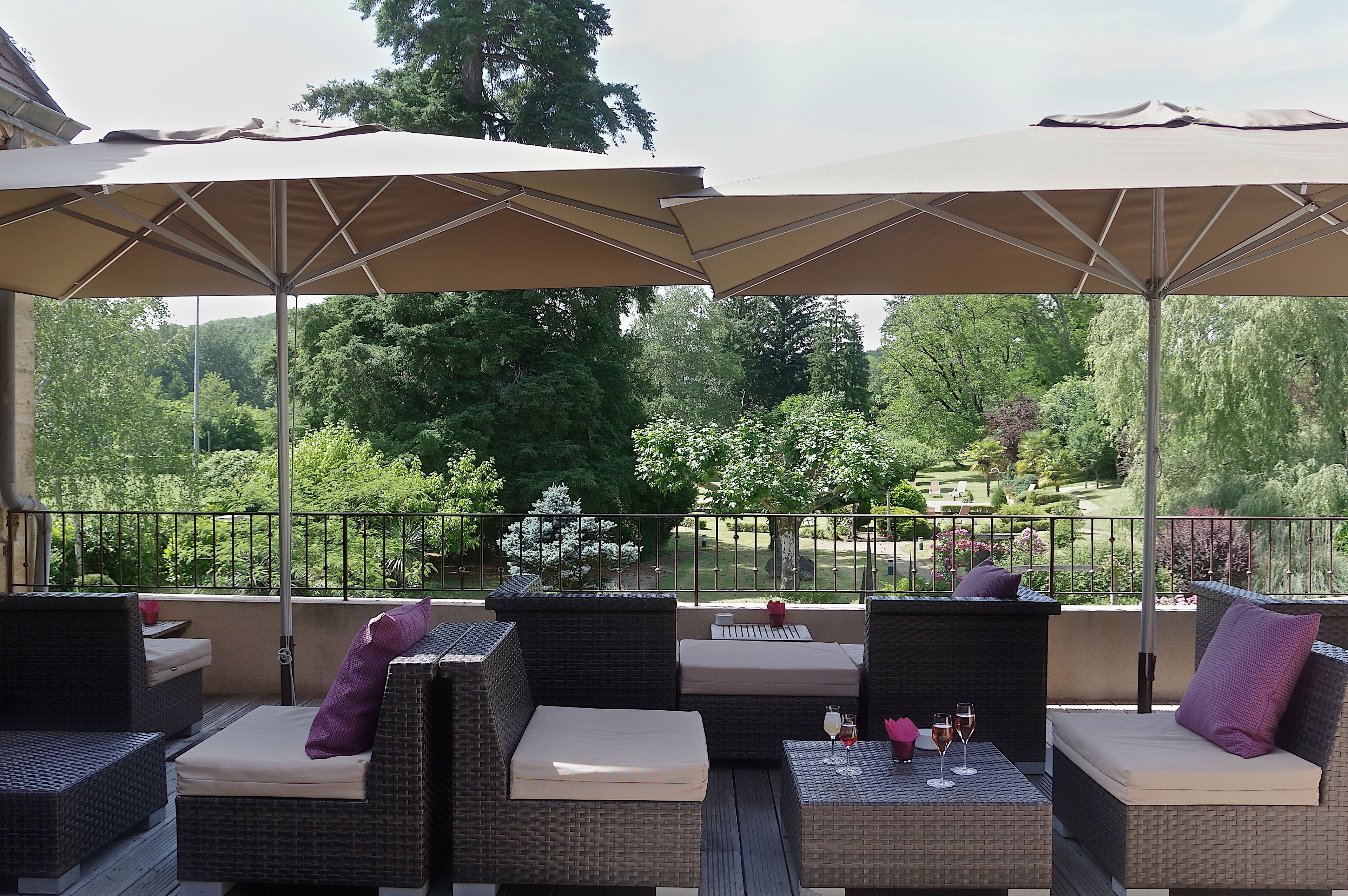 Una terrazza esterna con mobili in vimini, cuscini beige e ombrelloni che offrono ombra.