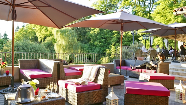 Un espacio al aire libre con patio, mobiliario de mimbre, cojines rojos y sombrillas.