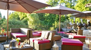 Un espace extérieur aménagé en terrasse, avec des meubles en osier, des coussins rouges et des parasols.