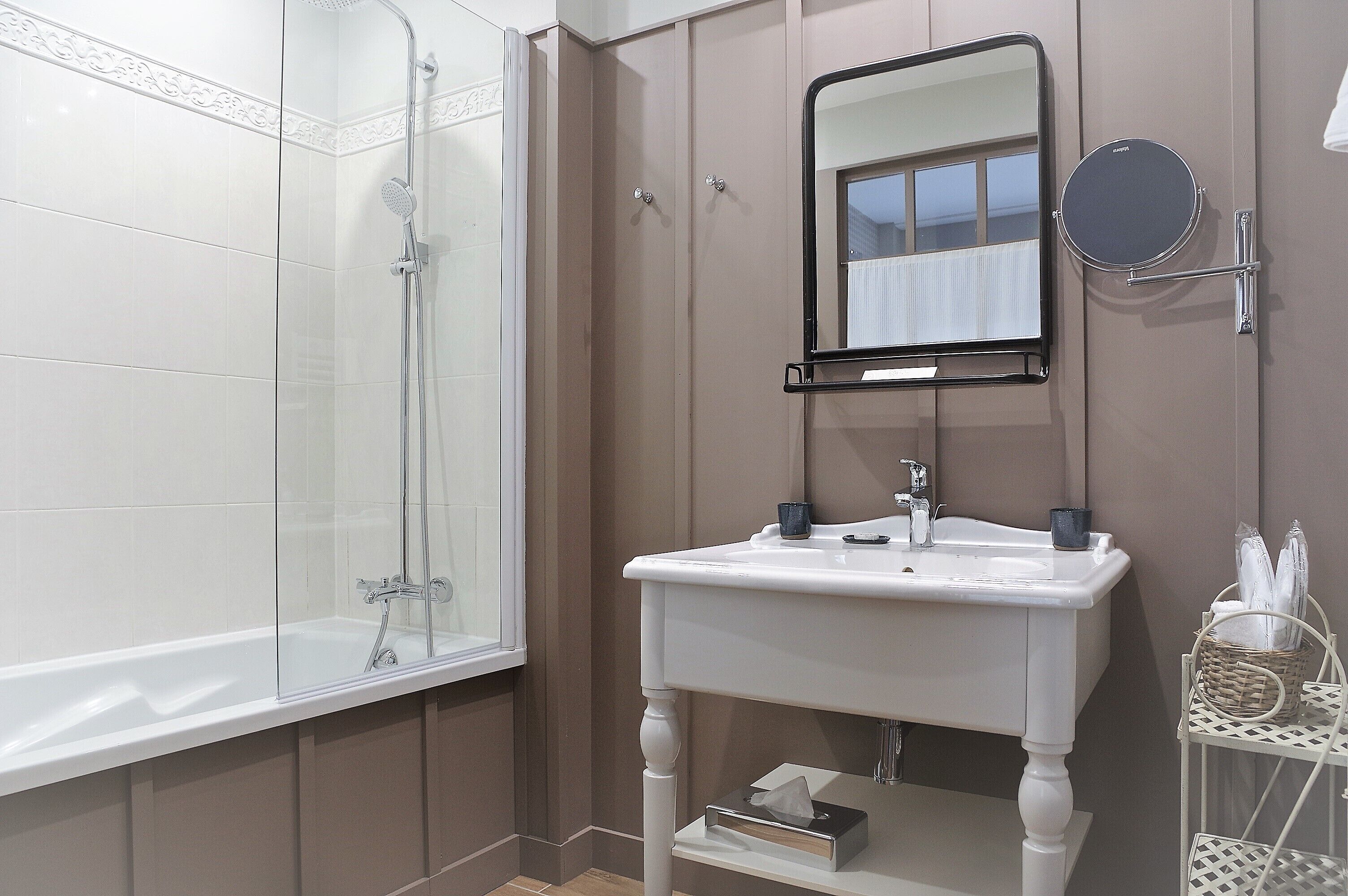 A bathroom with a glass-enclosed shower, a white sink with a mirror, and a small shelf with toiletries.