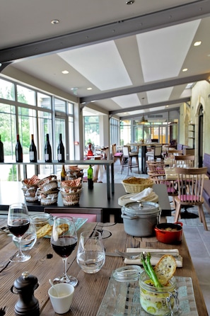 A restaurant with tables set for dining, wine glasses, and bottles on shelves. -  Les Glycines - Hôtel & Spa (Les Eyzies)