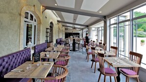 Un restaurante con mesas de madera, asientos tapizados en tono morado y amplios ventanales, además de una zona de bar.