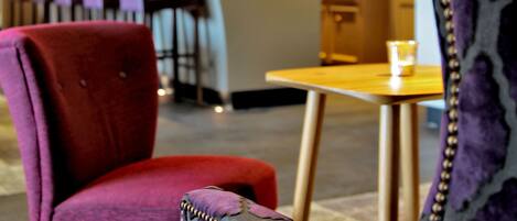 Een restaurantinterieur met een bar, rode en paarse stoelen met bekleding en hanglampen.