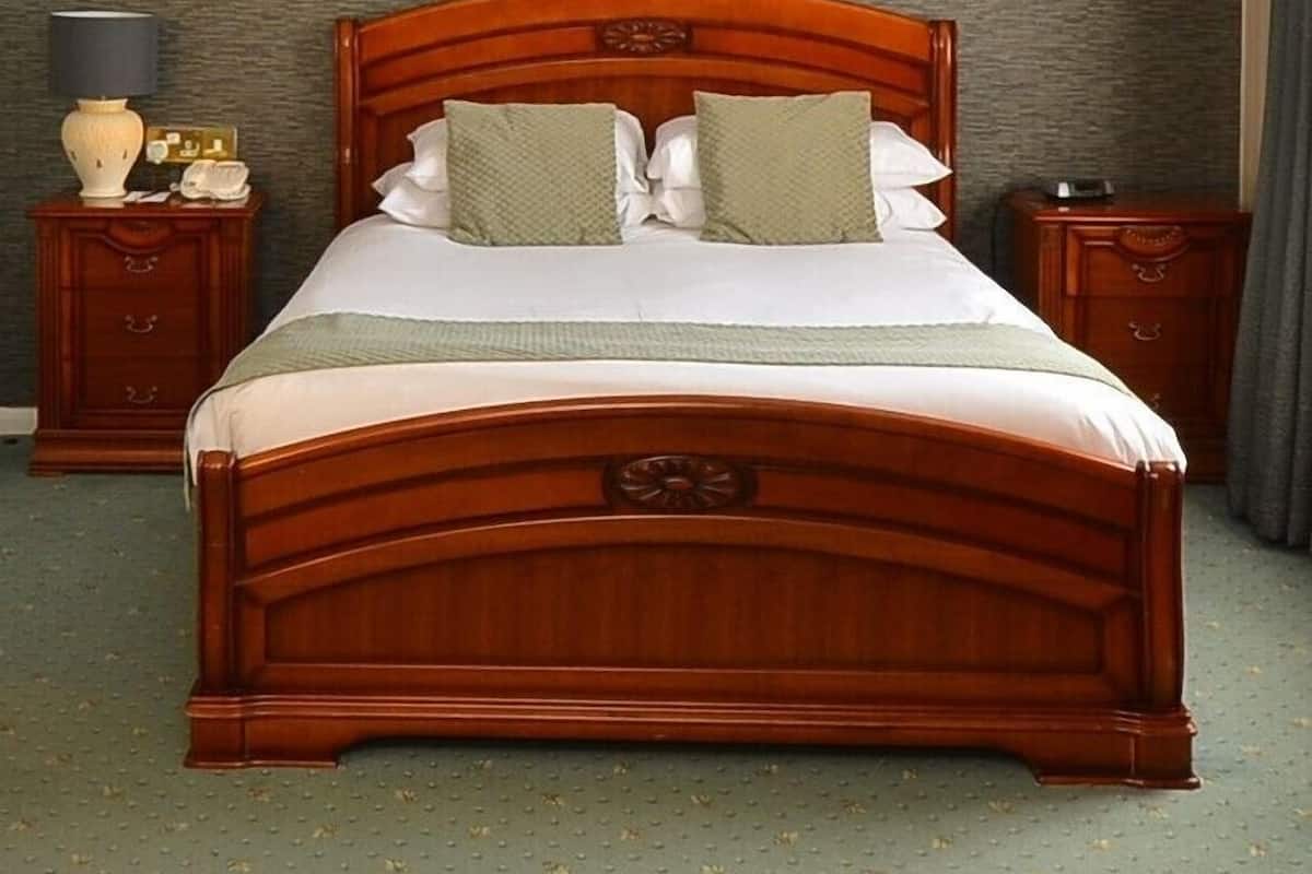 Uma cama bem arrumada com cabeceira de madeira, duas mesas de cabeceira com abajures e uma parede com textura.
