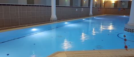 An indoor swimming pool with tiled walls, a tiled floor, and a ceiling with recessed lighting.