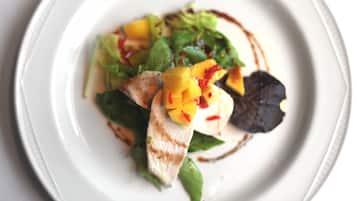 Un piatto bianco con un'insalata di verdure, mango a cubetti e guarnizione a foglia.
