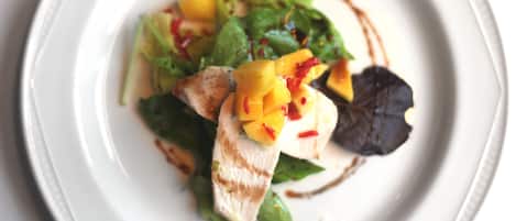 Un plato blanco con una ensalada de hojas verdes, trozos de mango y una guarnición de hojas.