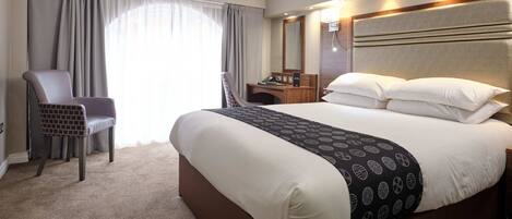 A hotel room with a large bed, a chair, a desk with a phone, and a mirror.