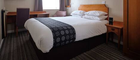 A hotel room with a bed, a desk, a chair, a television, and a window with curtains.