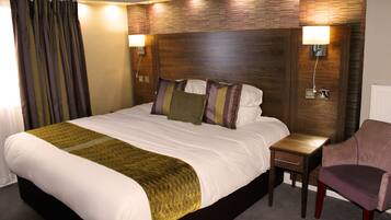 A hotel room with a large bed, bedside tables, a chair, and a wooden headboard.