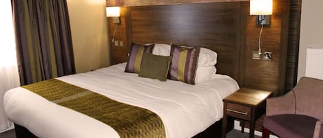 A hotel room with a large bed, bedside tables, a chair, and a wooden headboard.