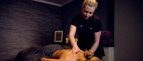 A massage therapy room with a massage table, a client receiving a back massage, and a wall-mounted massage table.