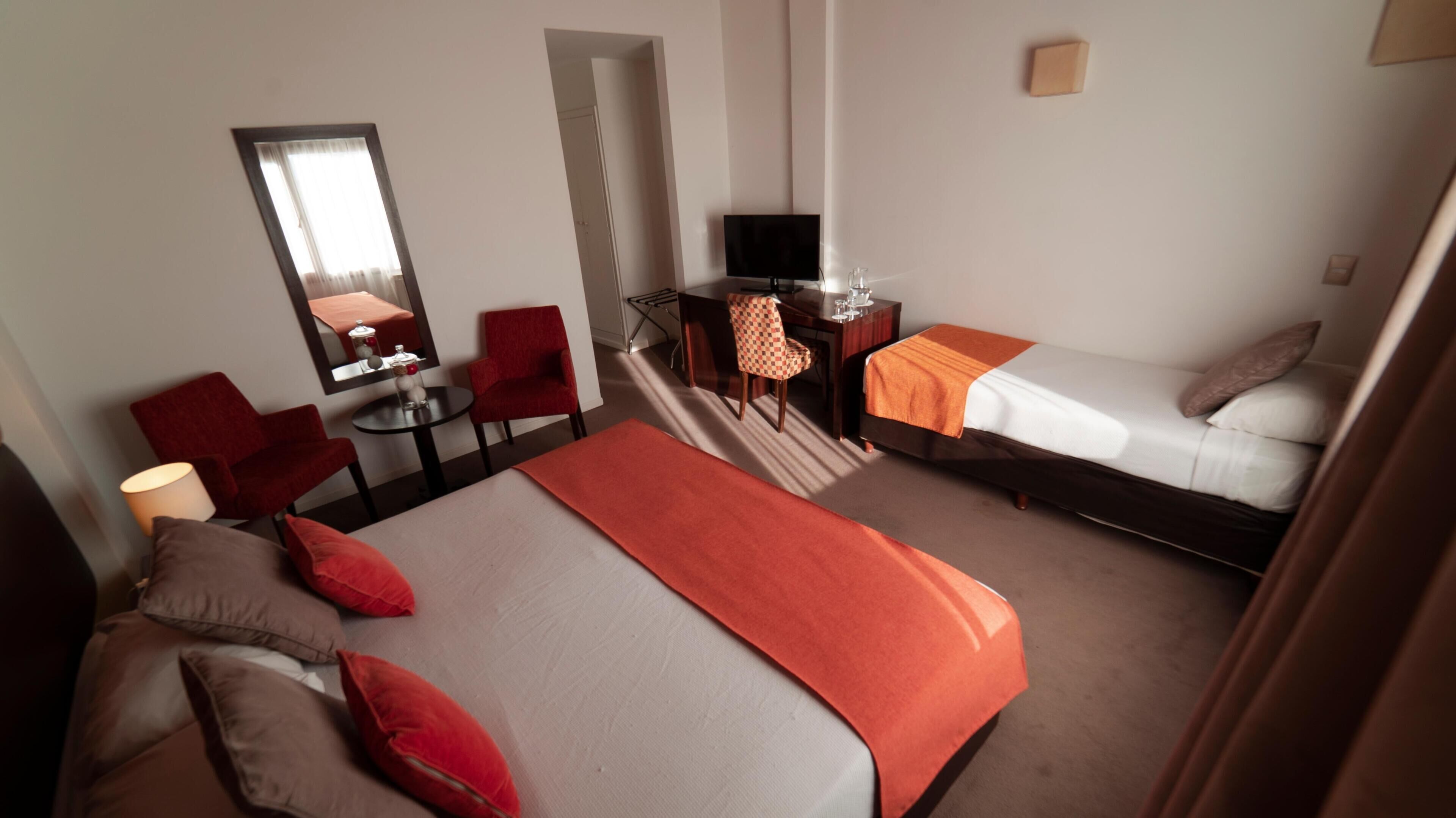Habitación de hotel con una cama, un escritorio con computadora, una silla, una mesita de noche con lámpara y un espejo en la pared.