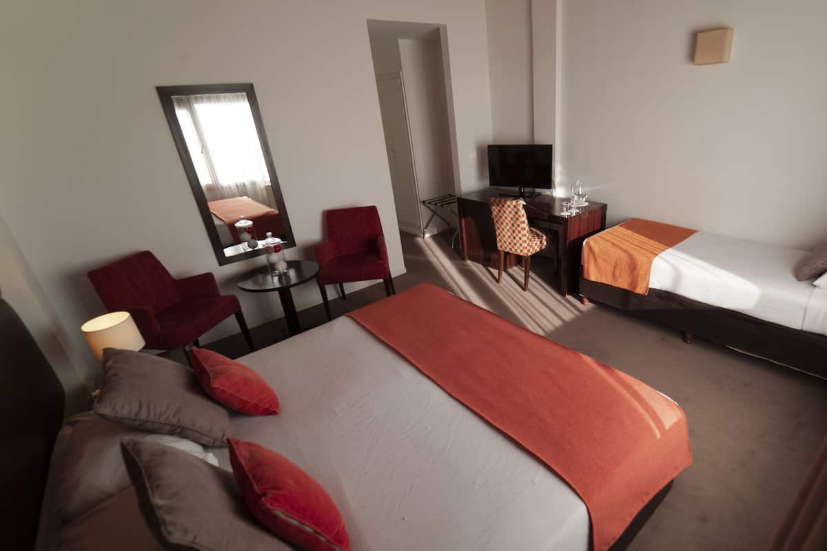 A hotel room with a large bed, a desk with a chair, a television, and a small table with a lamp.