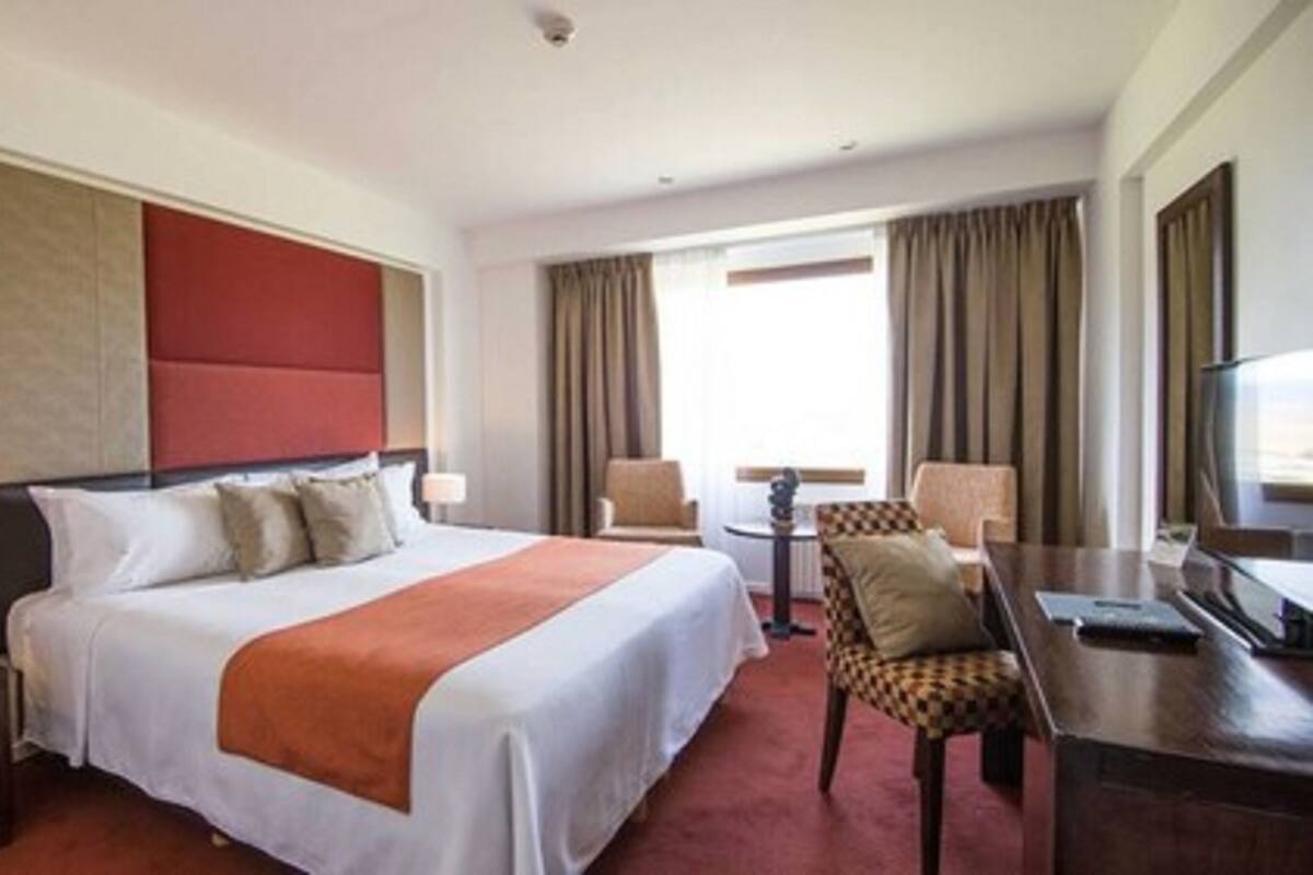 A hotel room with a large bed, a desk with a chair, a television, and a window with curtains.
