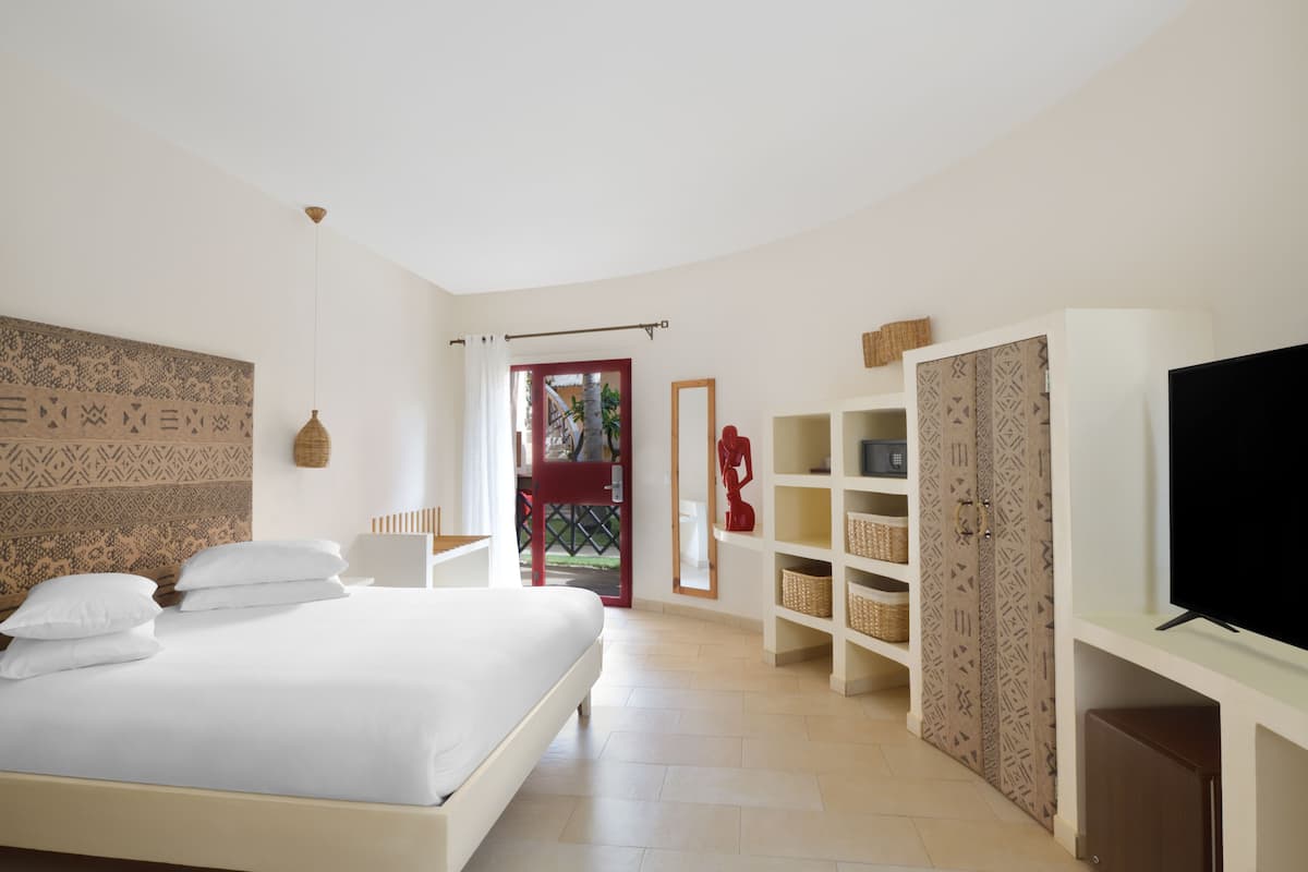 Quarto com cama, televisão, guarda-roupa e porta que dá para uma varanda.