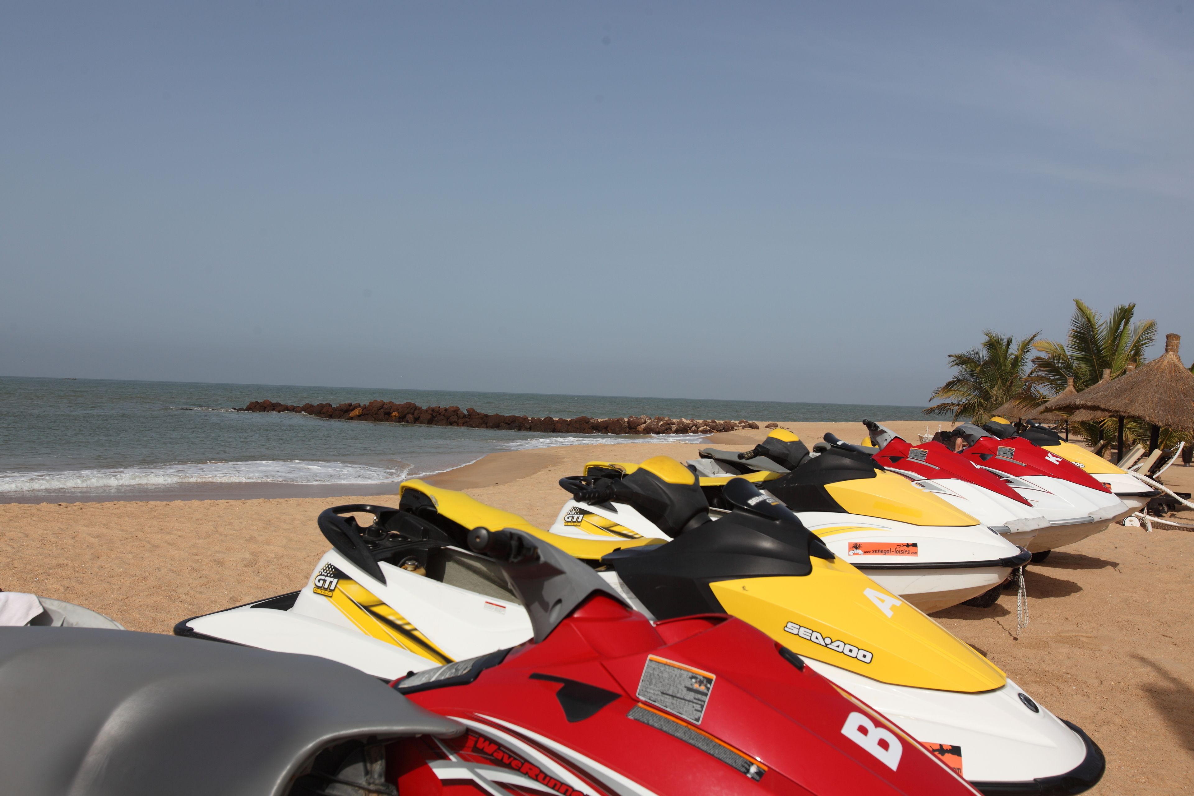 Una fila de motos acuáticas sobre una playa arenosa, con el océano al fondo.