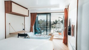 Una habitación de hotel moderna con cama, escritorio, silla, mesita pequeña, sillón colgante y vistas al exterior.