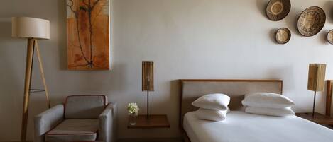 Una habitación de hotel moderna con una cama, un sofá, una mesita de noche, una lámpara y obras de arte en la pared.