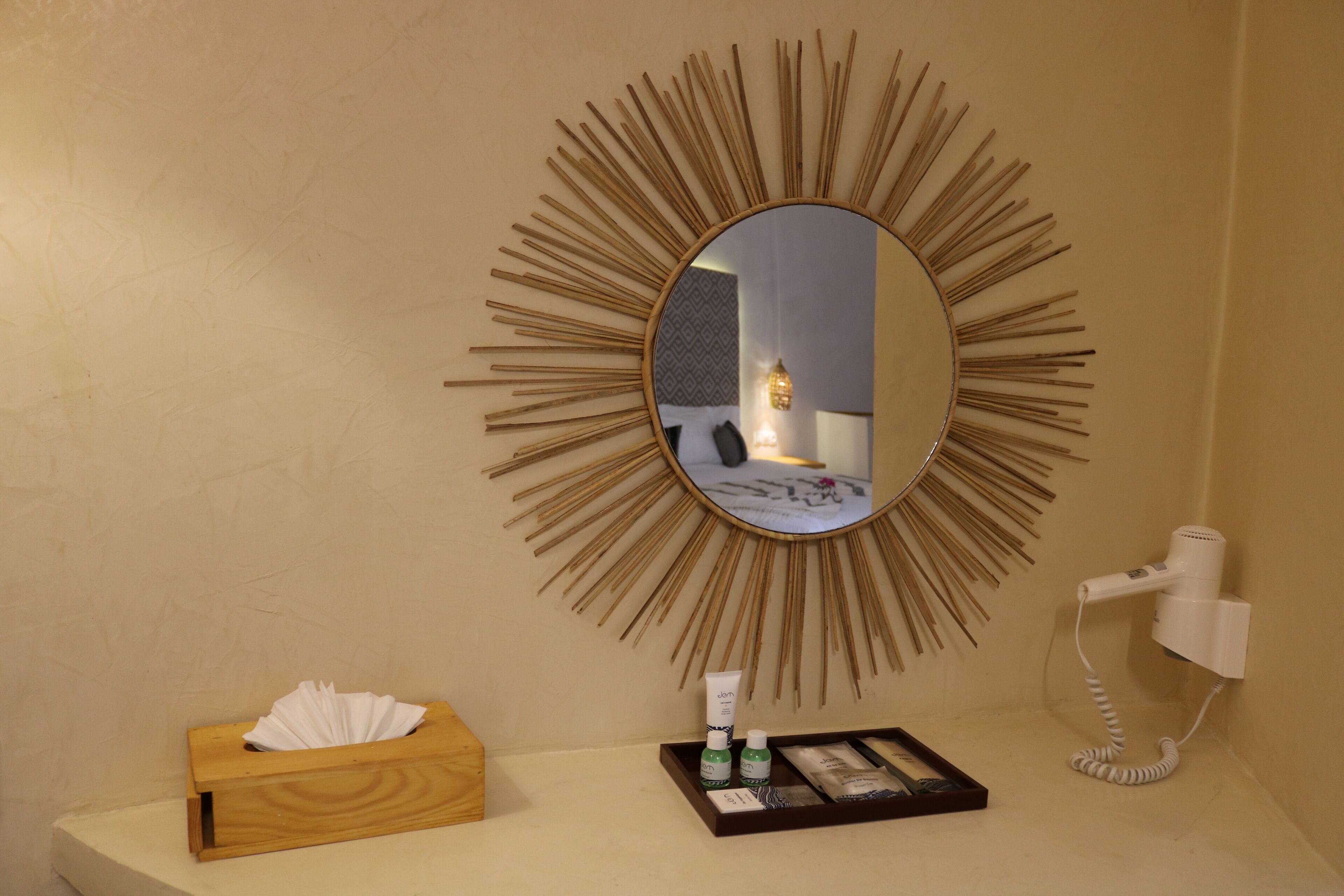 Une salle de bain avec un miroir rond, une boîte de mouchoirs, des articles de toilette et un sèche-cheveux.