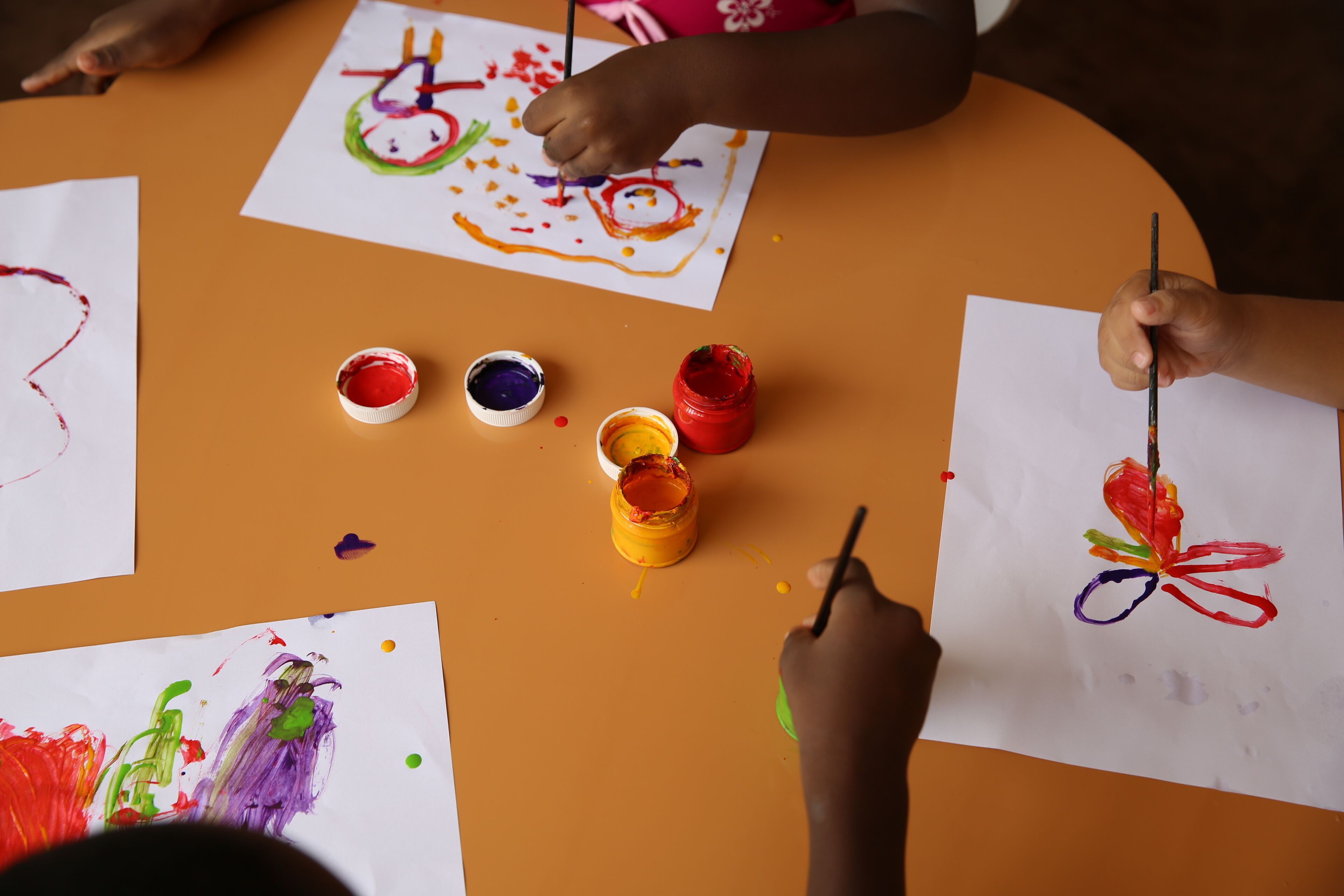 A table with children's artwork and paint containers.