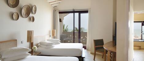 A hotel room with two beds, a wooden table, a chair, and a balcony with a view.