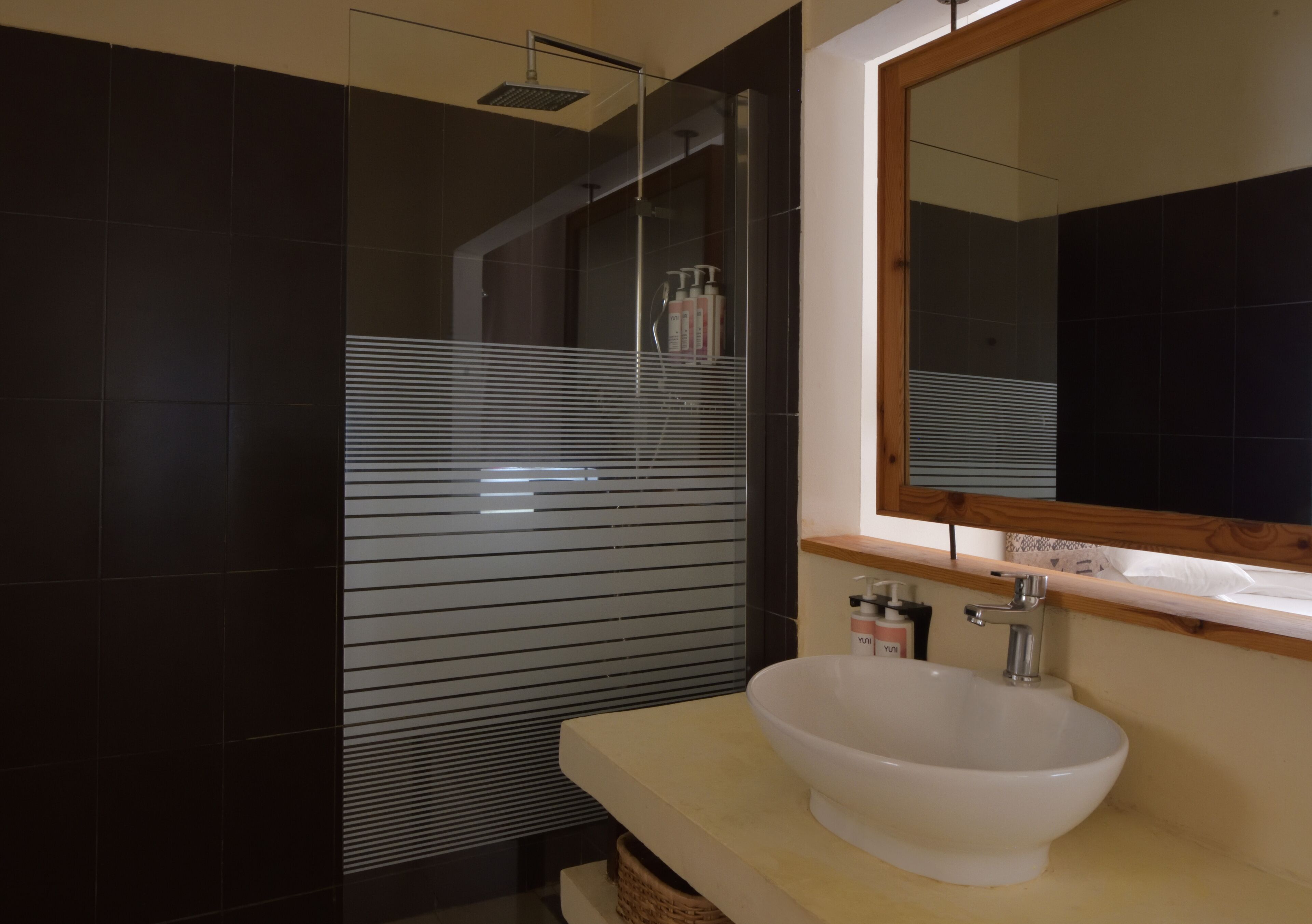 Un bagno moderno con un lavandino bianco ampio, uno specchio sopra e una cabina doccia con porta in vetro.