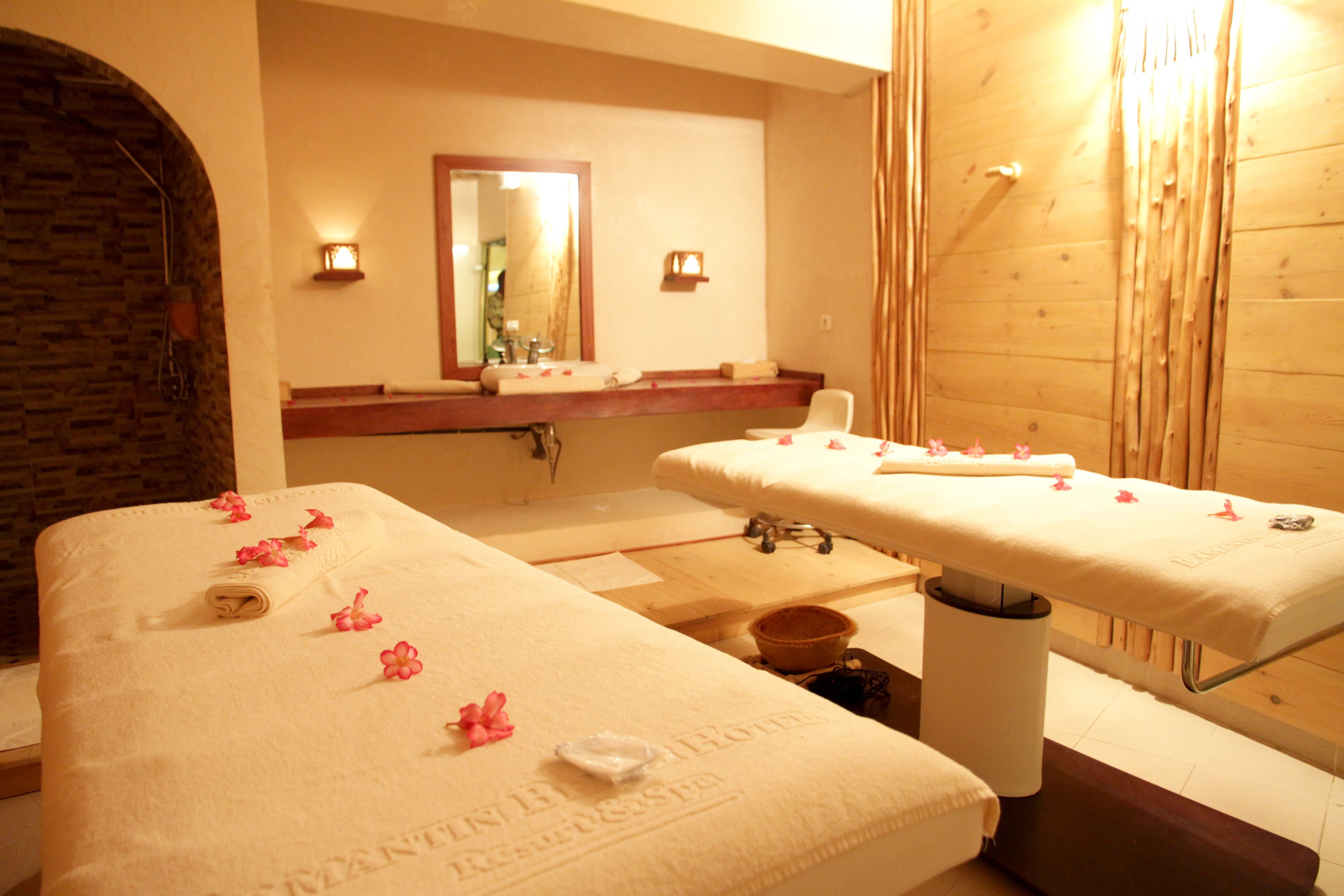 Ett spa-rum med två massagebänkar, en vägg av trä, en stenvalvbåge och en spegel ovanför handfatet.