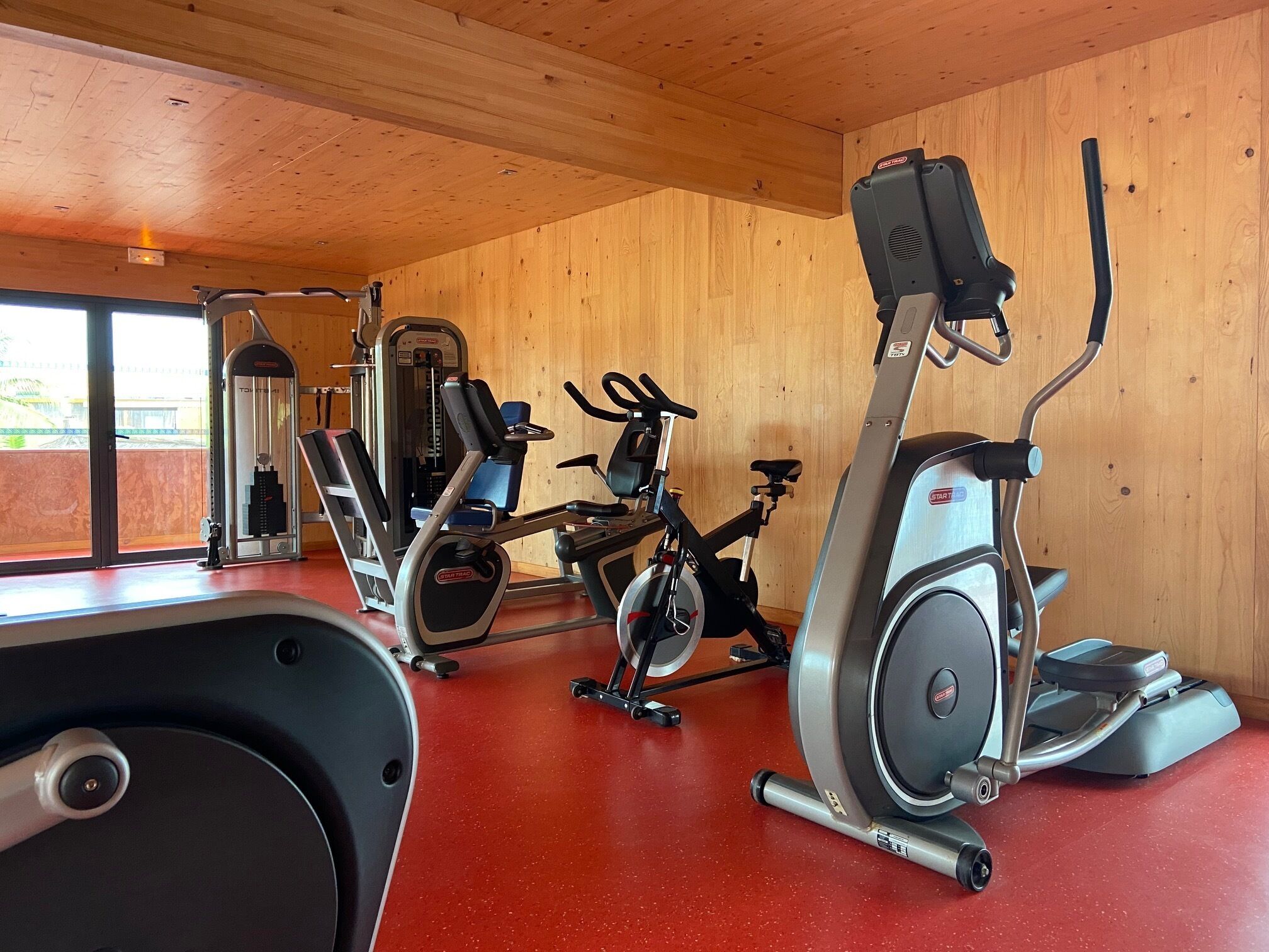 A gym with cardio machines, weight machines, and a red floor.