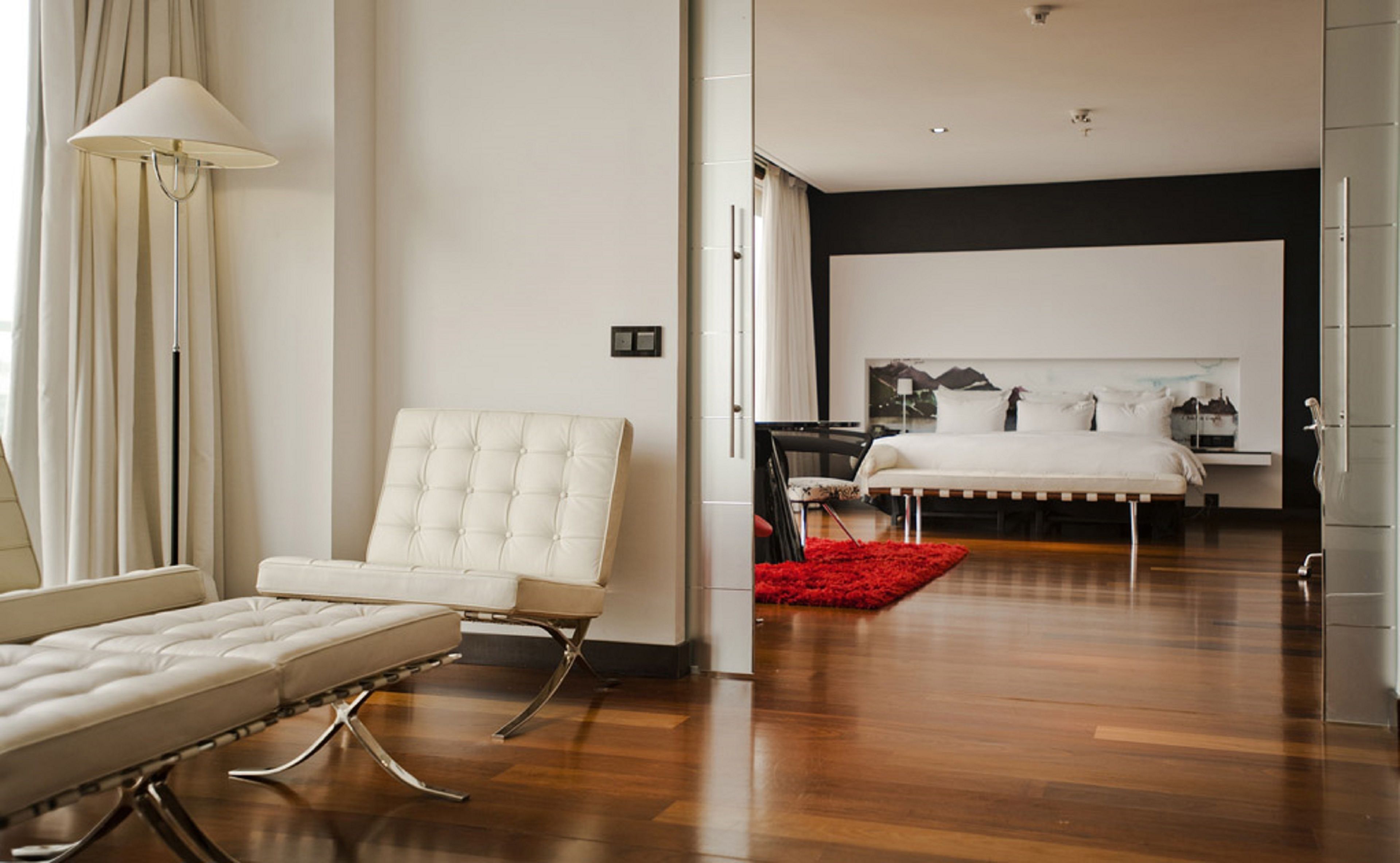 Une chambre moderne avec un grand lit, un coin salon comprenant un canapé et un fauteuil, et un tapis rouge.