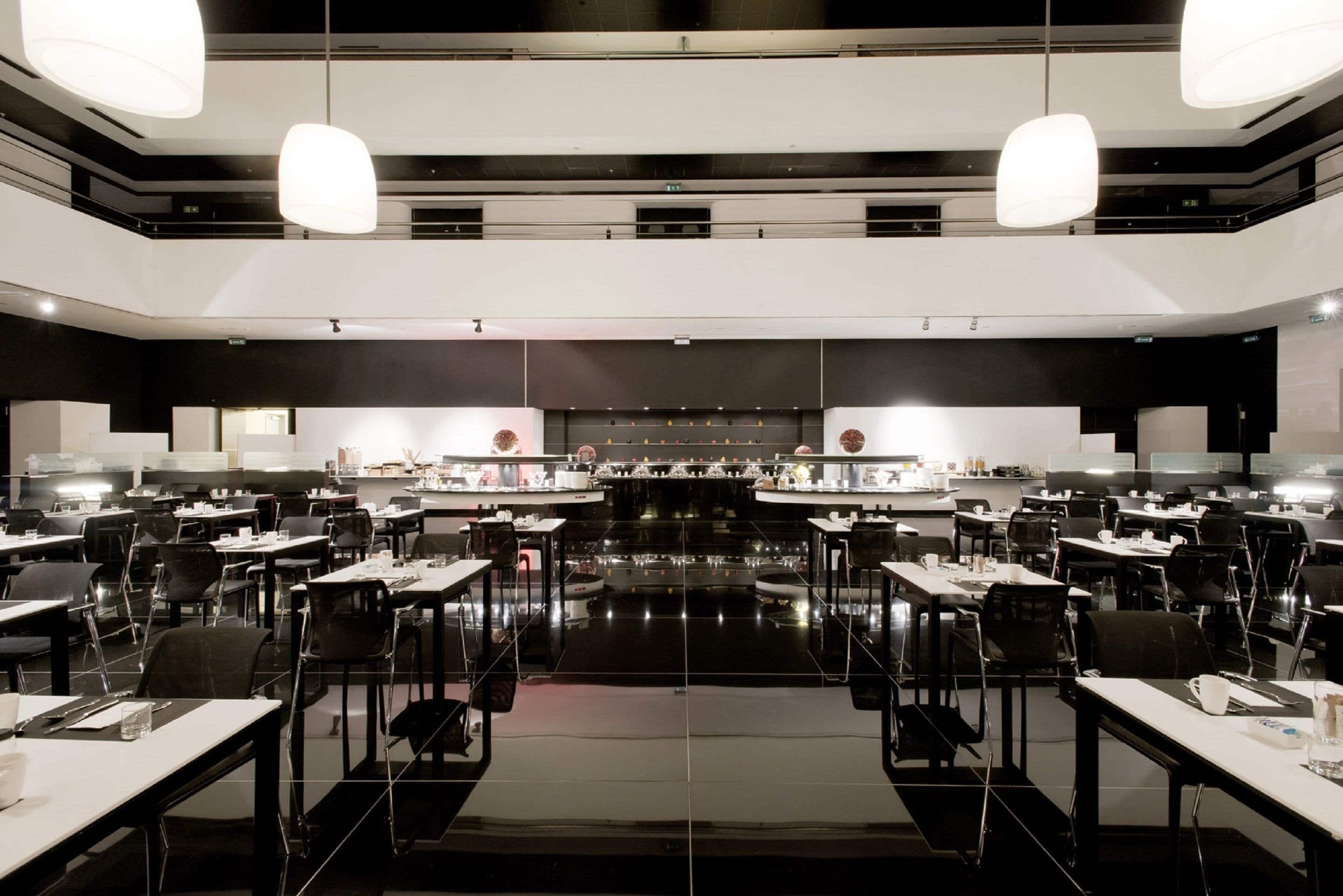 A modern dining area with multiple tables and chairs, overhead lighting, and a central counter.
