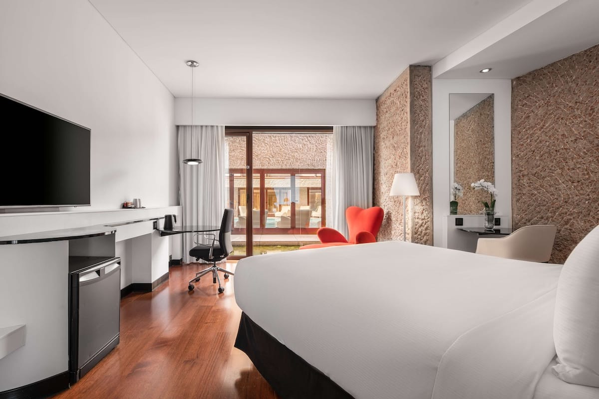Een moderne hotelkamer met een groot bed, een bureau met een flatscreen televisie, een stoel en uitzicht op de omgeving.