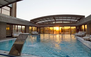 A rooftop pool with a glass balustrade, lounge chairs, and a view of the sunset.