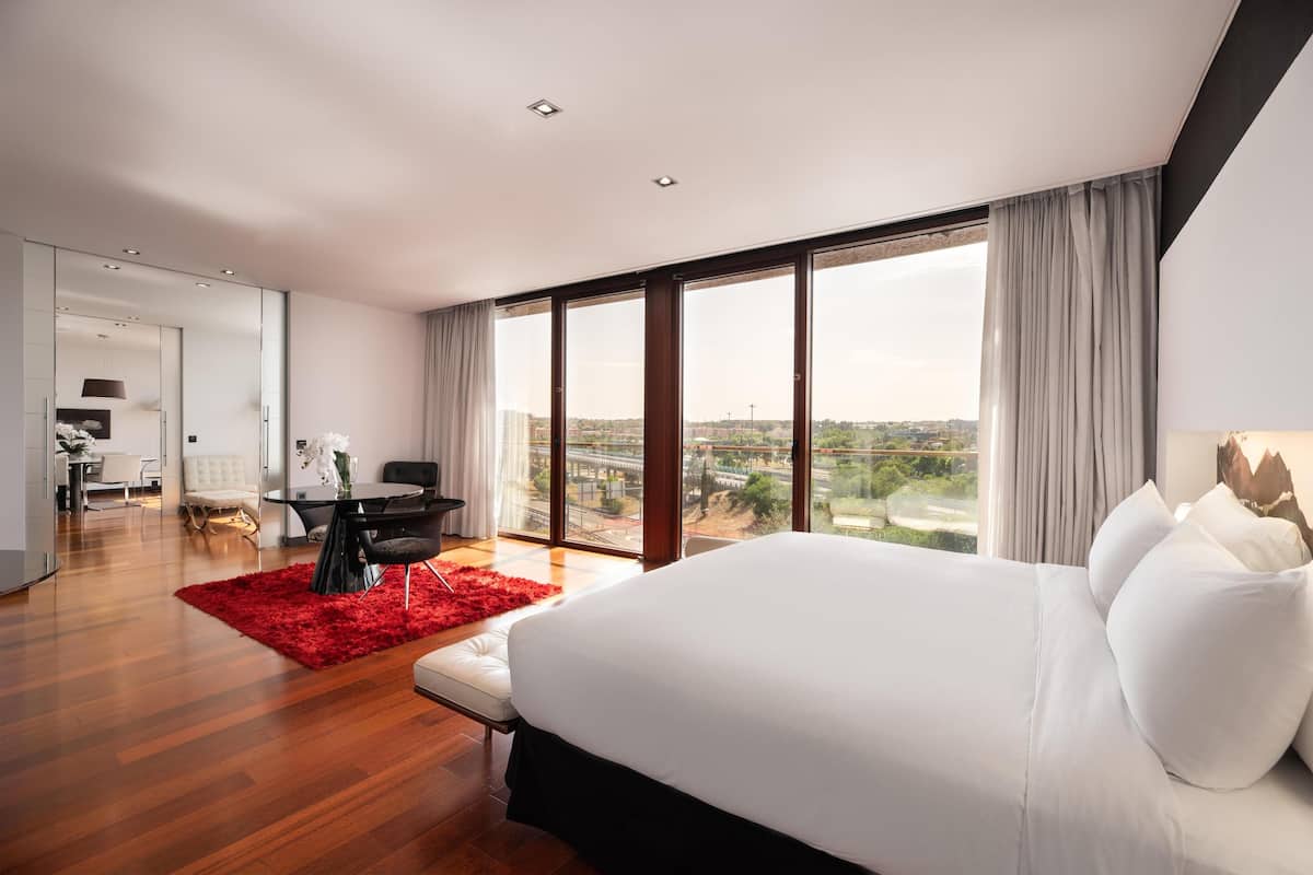Een moderne hotelkamer met een groot bed, een zithoek en uitzicht op de stadsbelangrijkste gebouwen.