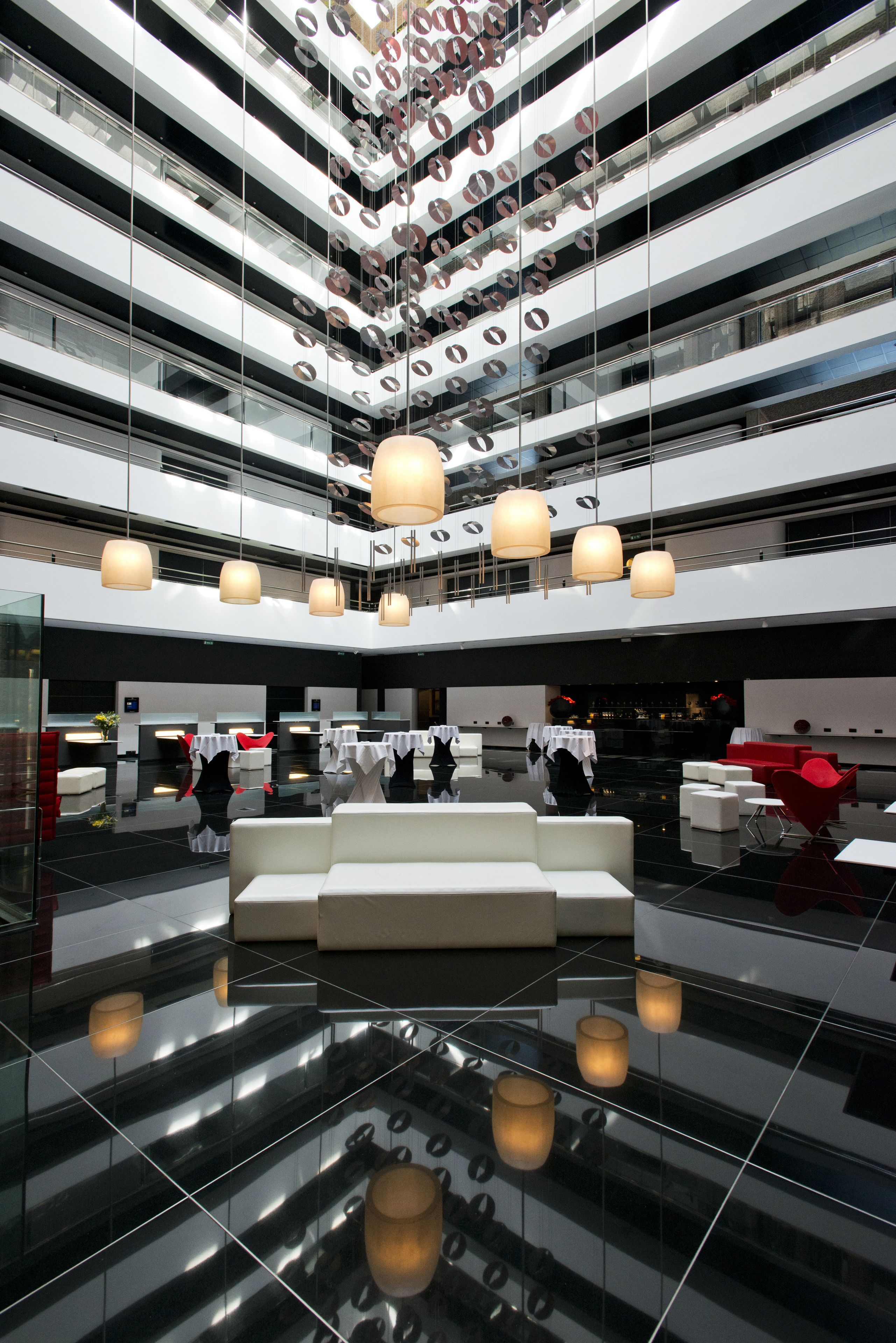 A modern hotel lobby with a reflective floor, multiple levels of balconies, and contemporary lighting fixtures.