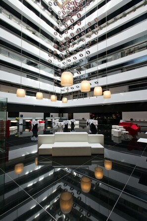 Un moderno vestíbulo de hotel con piso reflectante, varios niveles de balcones e iluminación contemporánea.